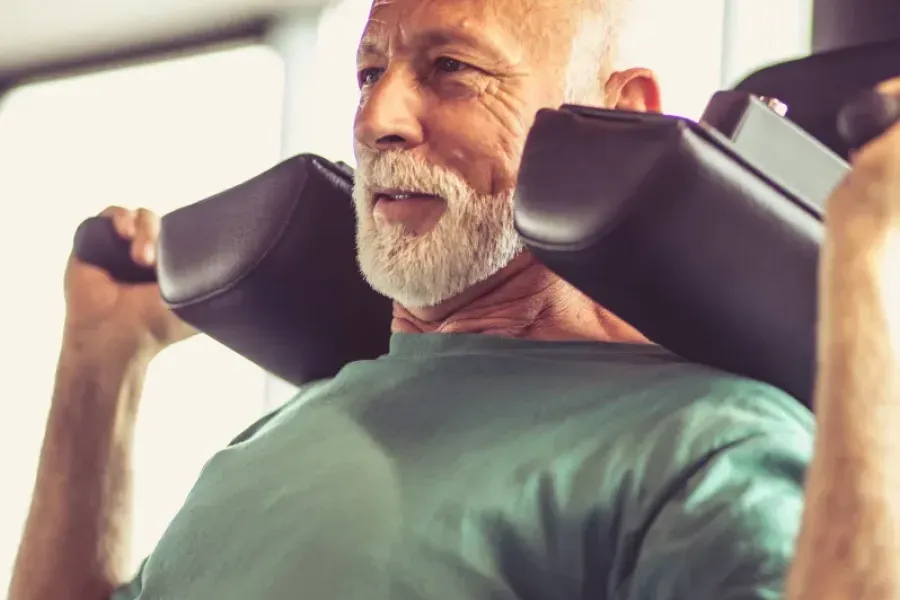 Acclaim at the Hill senior apartment homes with Older man exercising on a gym machine, wearing a green shirt, focused on his workout.