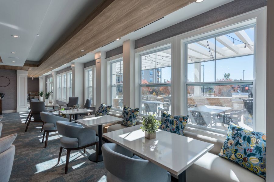 Acclaim at the Hill senior apartment homes with Modern dining area with white tables, blue chairs, and large windows overlooking an outdoor patio.
