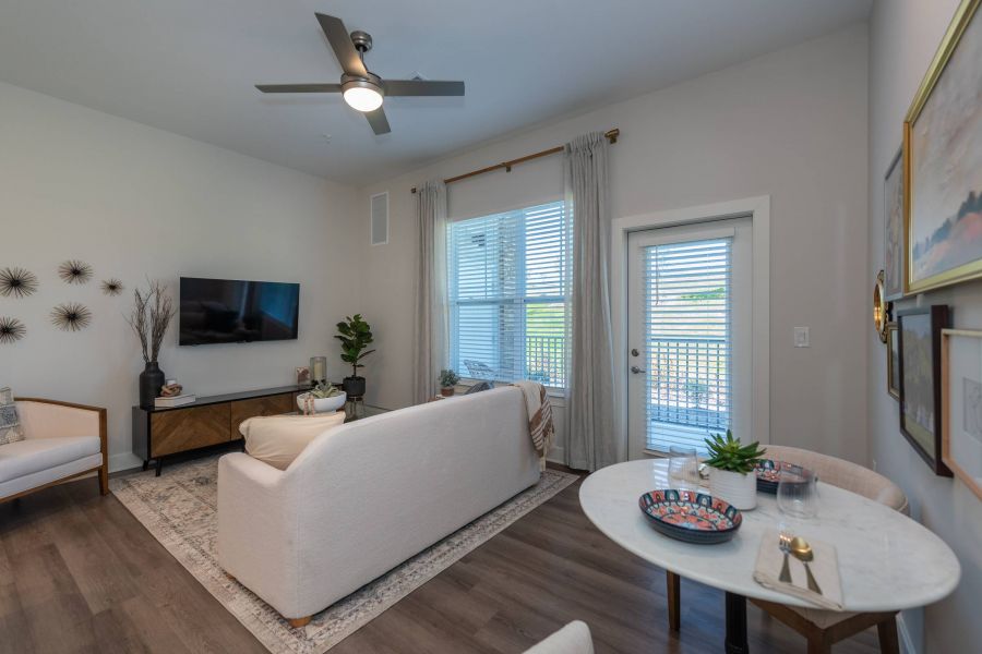 Acclaim at the Hill senior apartment homes with Modern living room with a sofa, TV, wall art, large window, and a small dining table with decor.