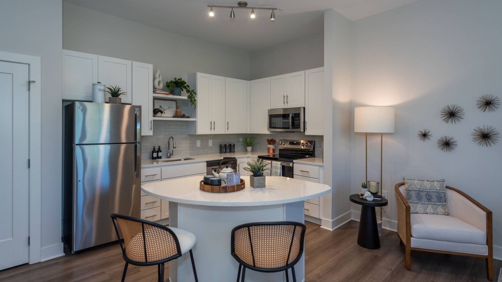 Modern kitchen and living area with white cabinets, stainless steel appliances, and a large island. Cozy seating area with a sofa and rug in the background. Bright and inviting atmosphere.