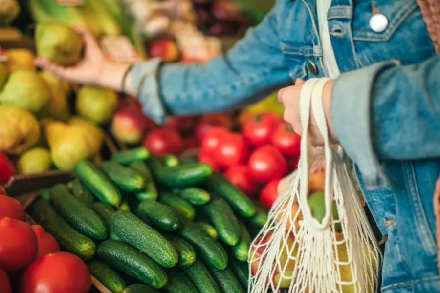 Acclaim at the Hill senior apartment homes with Person in a denim jacket picking fruit at a market with cucumbers and tomatoes in the foreground.