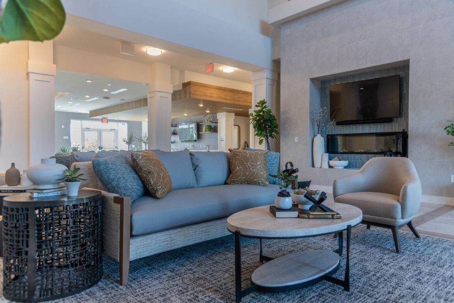 Acclaim at the Hill senior apartment homes with Modern living room with a gray sofa, armchair, coffee table, and a TV mounted above a fireplace.