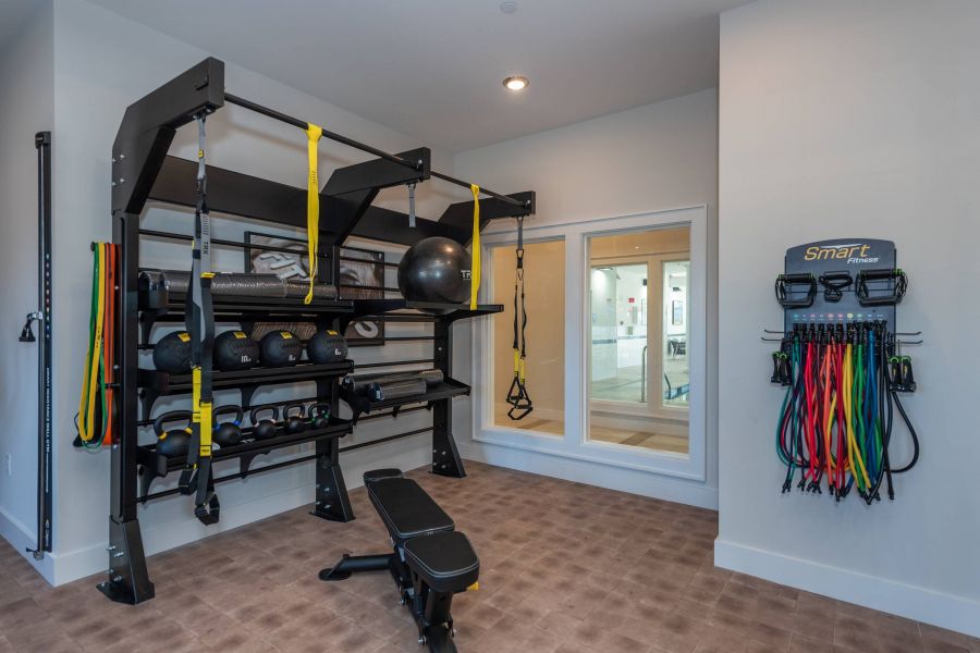 Acclaim at the Hill senior apartment homes with Home gym with weights, exercise bands, a bench, medicine balls, and a window to another room.