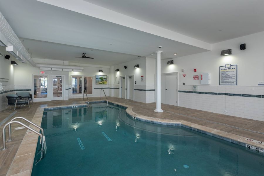 Acclaim at the Hill senior apartment homes with Indoor swimming pool with tiled deck, safety signs, and seating area under bright ceiling lights.