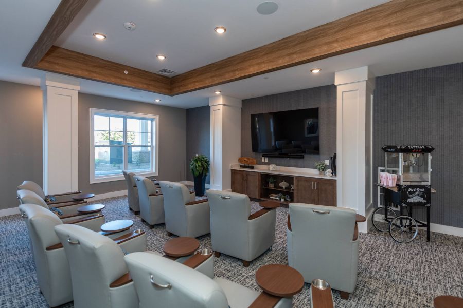 Acclaim at the Hill senior apartment homes with Small home theater room with gray chairs, a large TV, and a popcorn machine by the wall.