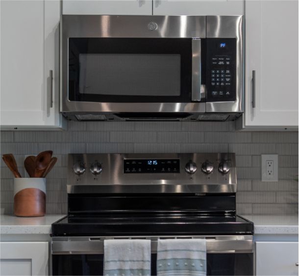 Acclaim at the Hill senior apartment homes with Stainless steel microwave above a stove in a modern kitchen with a towel hanging on the oven handle.
