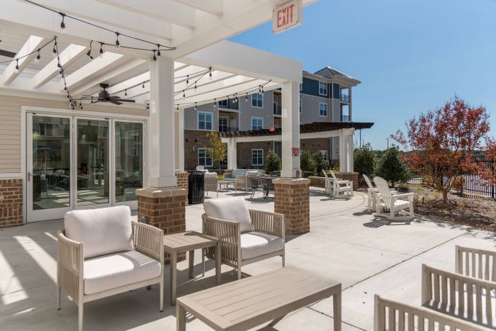 Acclaim at the Hill senior apartment homes with Outdoor patio with white pergola, cushioned chairs, string lights, and a view of apartment buildings.