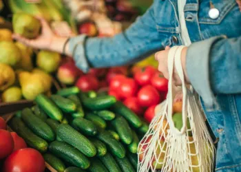 Acclaim at the Hill senior apartment homes with Person in a denim jacket picking fruit at a market with cucumbers and tomatoes in the foreground.