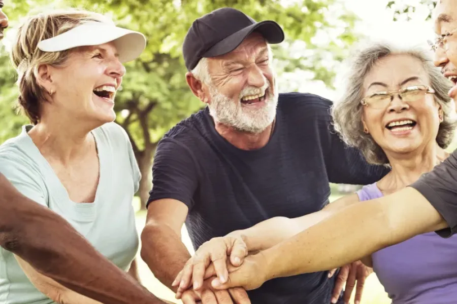Acclaim at the Hill senior apartment homes with Group of smiling seniors outdoors, stacking hands in a circle, enjoying a joyful moment together.