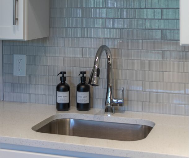 Acclaim at the Hill senior apartment homes with Modern kitchen sink with chrome faucet, soap dispensers, and light gray tile backsplash on a white countertop.