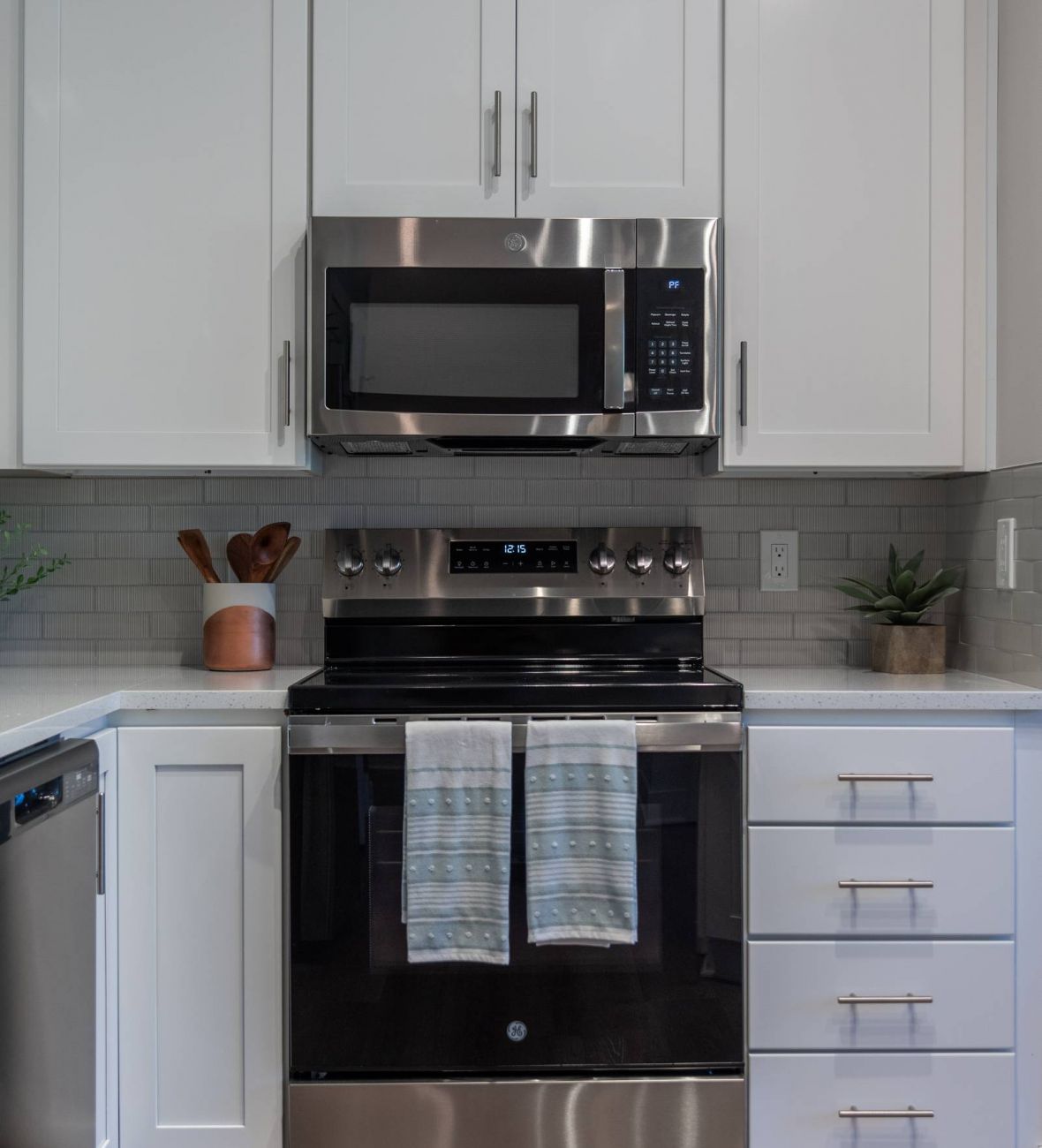 Acclaim at the Hill senior apartment homes with Modern kitchen with white cabinets, a stainless steel oven and microwave, and two towels hanging on the oven.