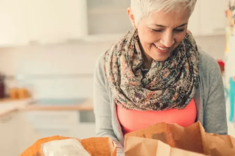 Acclaim at the Hill senior apartment homes with Smiling woman with short gray hair and scarf unpacking groceries in a bright kitchen.