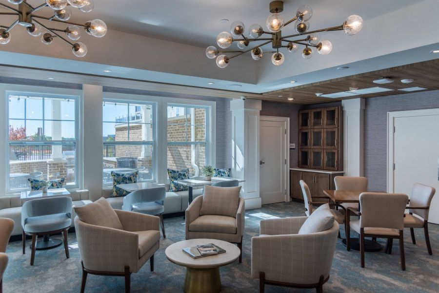 Acclaim at the Hill senior apartment homes with Modern lounge with armchairs, tables, large windows, and stylish light fixtures, in a bright, inviting space.