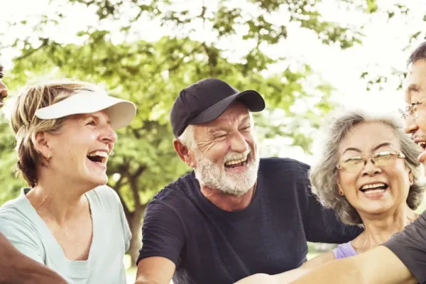 Acclaim at the Hill senior apartment homes with Group of smiling seniors outdoors, stacking hands in a circle, enjoying a joyful moment together.