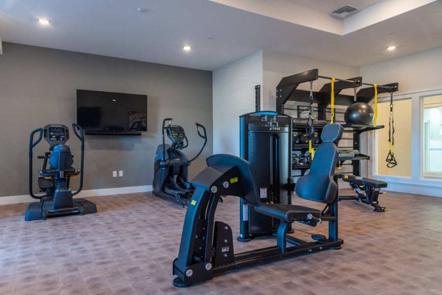 Acclaim at the Hill senior apartment homes with Modern gym room with cardio machines, strength equipment, and wall-mounted TV on gray walls.