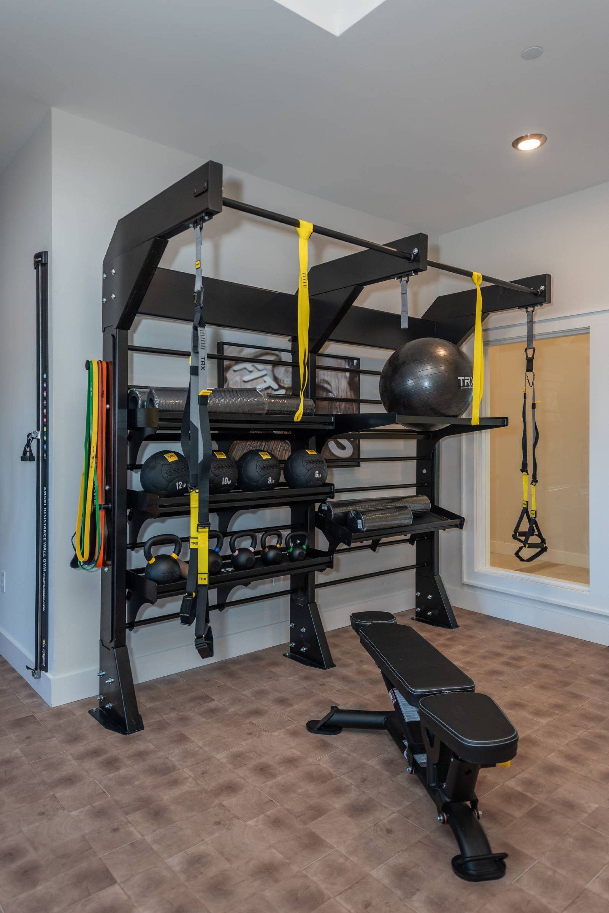 Acclaim at the Hill senior apartment homes with Home gym with weights, resistance bands, TRX straps, exercise balls, and a workout bench on a tiled floor.