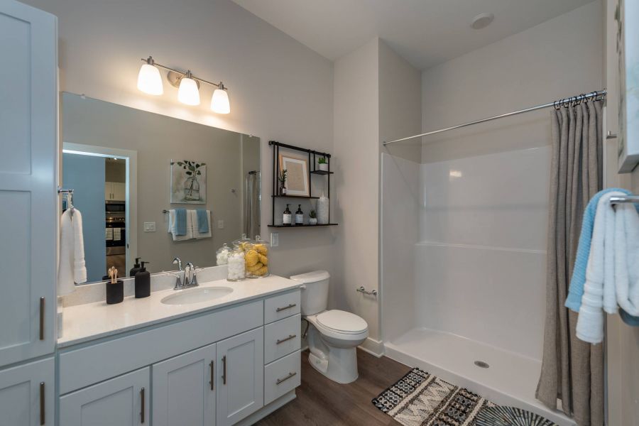 Acclaim at the Hill senior apartment homes with Modern bathroom with white cabinets, a large mirror, walk-in shower, and decorative towels and rugs.