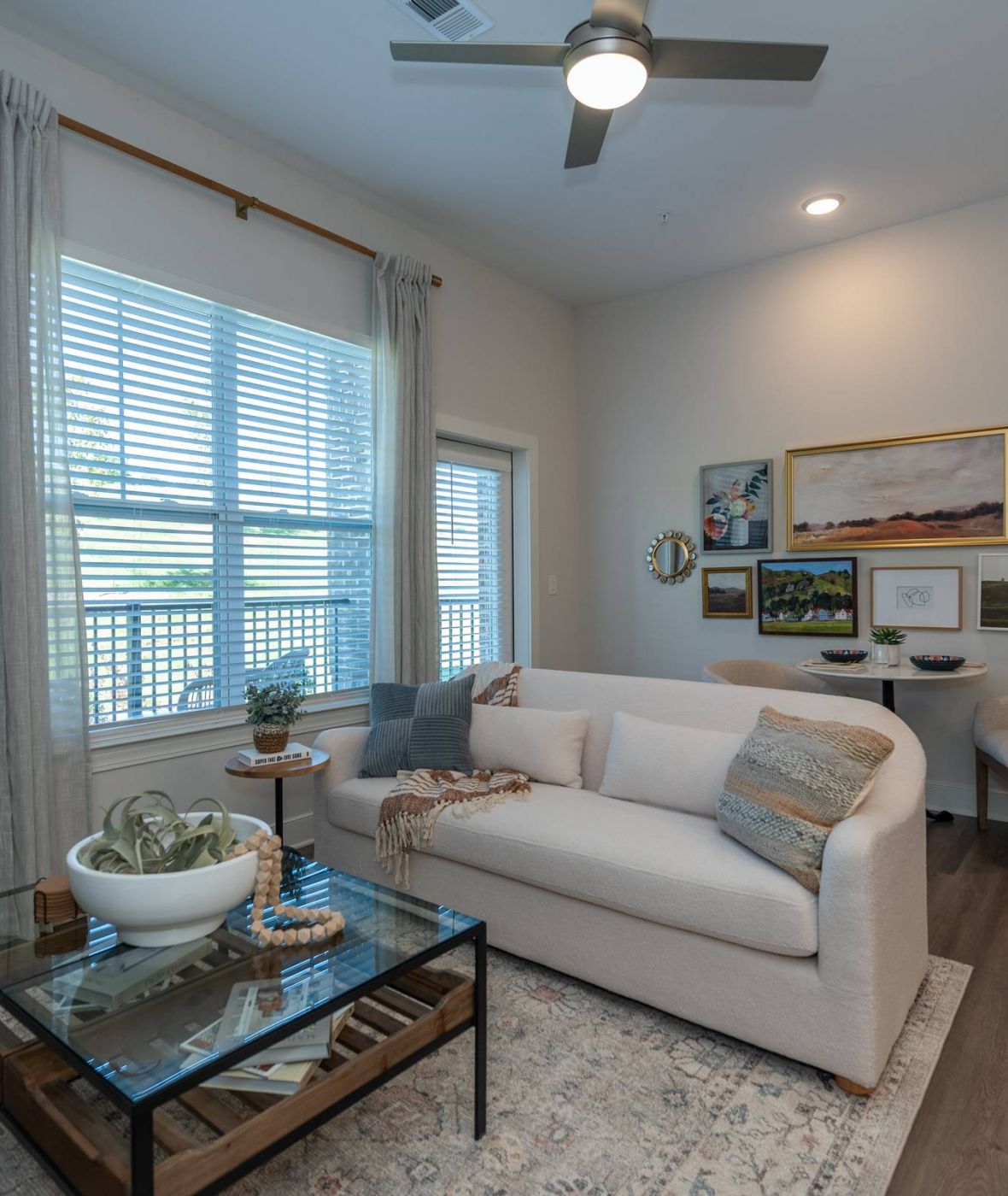 Acclaim at the Hill senior apartment homes with Modern living room with a white sofa, glass coffee table, wall art, and window with gray curtains.